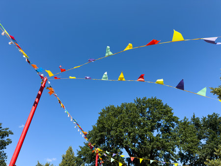Colorful festive pennant flags stretched on strings between red poles against clear blue summer sky...