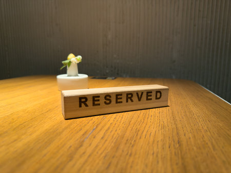 Wooden reserved sign on table in a restaurant, modern interior with a small flower decoration, symbolizing reserved seating for customers or guestsの写真素材