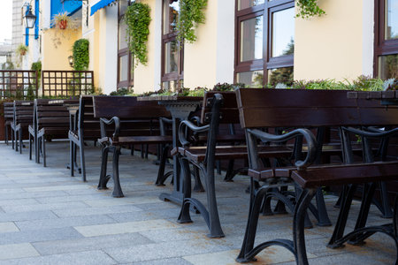 Peaceful outdoor cafe scene with benches and tables under the shade, creating the perfect space for relaxation. Neat arrangement and surrounding greenery invite guests to enjoy urban diningの写真素材