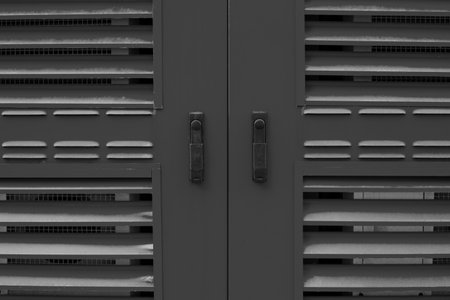 Close up black and white photo of ventilation cabinet with slatted panels and locks. Photo emphasizes industrial design, smooth texture of metal, and simplicity of functional architectureの写真素材