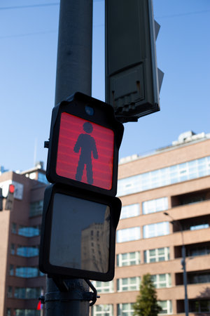 Red pedestrian traffic light in urban setting indicating stop, captured with clear digital technology. Traffic signal is prominently displayed against bright blue sky and modern city buildingsの写真素材