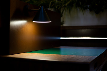 Dimly lit workspace with focused beam of light on green table, showcasing modern and minimalist...