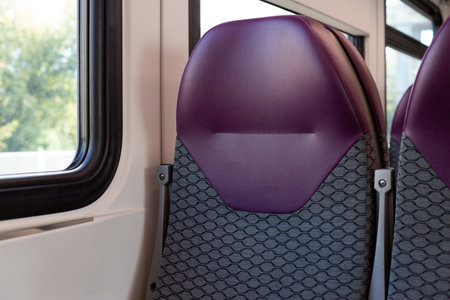Close up of train seats, with focus on purple colored headrest and patterned seat design. Window frame and outdoors are visible in the background, suggesting travel or transportation theme.の写真素材