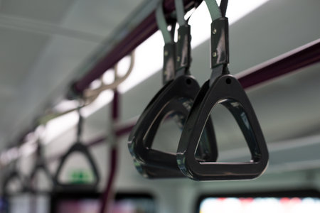 Close up photograph showing triangular hand straps hanging from ceiling, typical in modern train interior, with minimalistic lighting and clean designの写真素材