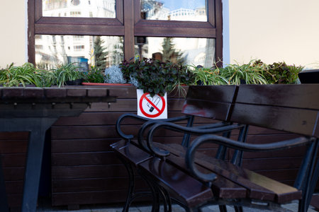 No smoking sign on table in front of building, with benches and plants around it, emphasizing the importance of maintaining clean and smoke free outdoor spaces for visitorsの写真素材