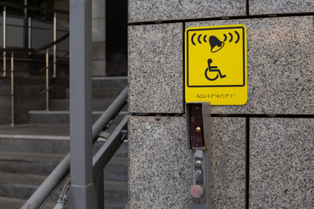 Yellow accessibility sign. Indicates call system with bell and is positioned on wall near stairs, with visible button to activate system. Offering assistance in public spacesの写真素材