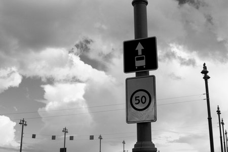 Black and white image of two road signs. One indicating bus lane and other showing speed limit of 50. Dramatic sky with clouds adds to photo atmosphereの写真素材