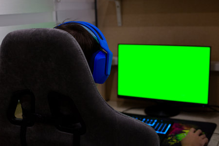 Background for a project about the computer industry. A gamer wearing headphones sits in a gaming chair in front of a monitor. Video games and working on a computer from homeの写真素材