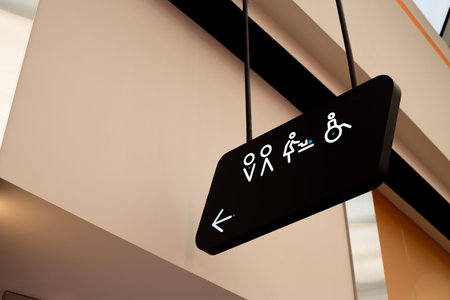 Hanging sign in public place with arrow pointing to restrooms for men, women and people with disabilities, as well as changing room for mothers and babies with diaper changing tableの写真素材