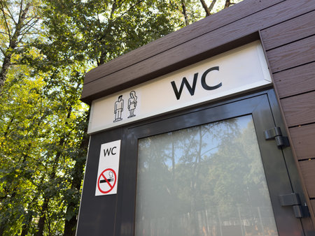 Sign above door of modern outdoor restroom in park with gender symbols. Public restroom outside with forest background. Universal orientation signs on street wc for people comfortの写真素材