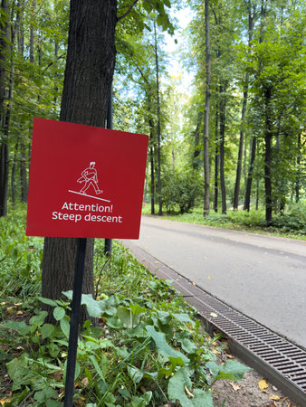 Public park with sign warning of steep descent. The risk of falling and injury during descent. The dangers of poor terrain and injury prevention. Keeping people safe while walking uses warning signsの写真素材