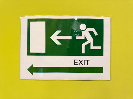 Green sign on yellow wall with building exit direction. Safe navigation indoors in case of fire or...