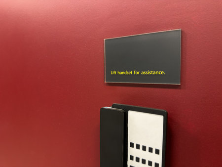 Lift handset for assistance. Wall mounted telephone in building with sign notifying availability of...