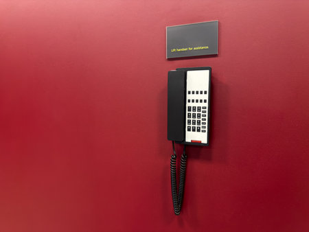Public telephone on red wall. Wall mounted phone for contacting operator against bright wall for text. Project about contacting operator using landline phoneの写真素材