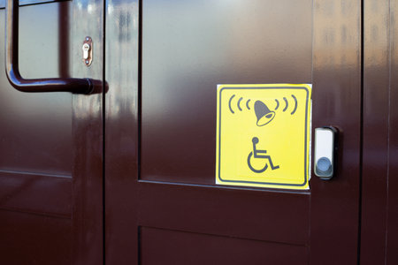 Yellow square sticker with symbol of person in wheelchair and bell next to the panel. Button for...