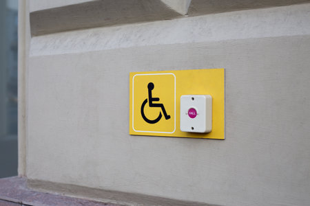 Yellow plastic panel to attract the attention of people with disabilities. Visible panel with wheelchair symbol and call button for assistance at the entrance to accessible buildingの写真素材