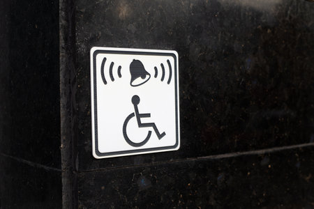 Black wall with white sign of person in wheelchair and bell symbol symbolizes accessible environment...