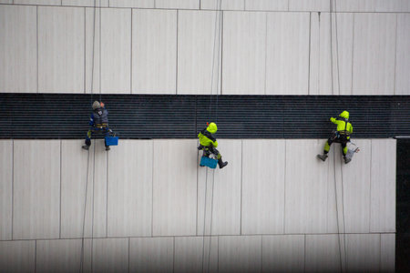 The most dangerous job in the world. Workers at height clean buildings in harsh weather conditions. Dangerous combination of height and bad weather. Risk job, industrial climbers at workの写真素材