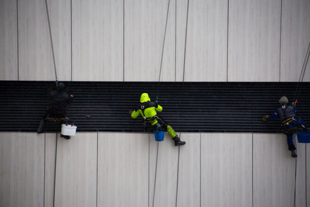 Industrial climbers wipe down building facade element with cloth. Climbers work at height. Safety equipment is essential for dangerous, life threatening workの写真素材