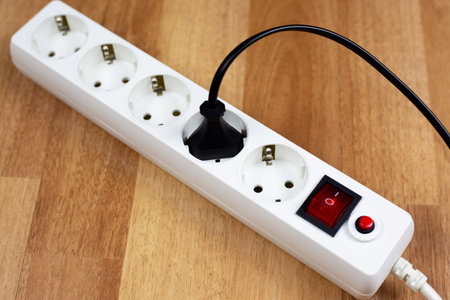 White power strip with red master switch sits on wooden surface. Black appliance plug is inserted...