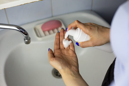 Woman squeezes skincare foam onto her hand from dispenser bottle. Using skincare product. Women...