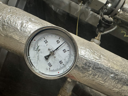 Pressure gauge attached to insulated metal piping in an industrial environment, showing readings...