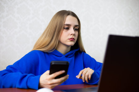Young woman compares prices on laptop and smartphone while shopping online. She searches for the...