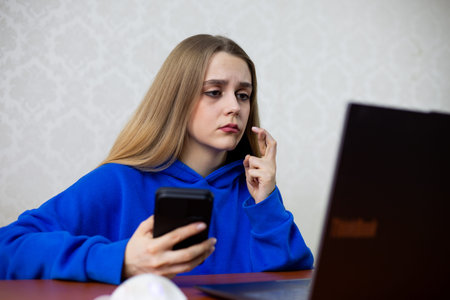 Hopeful blonde girl crosses fingers for luck while checking sports bet on laptop. She holds the...