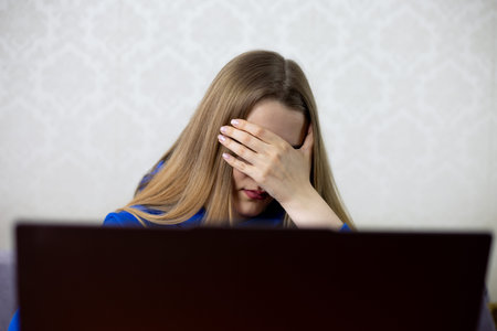 Frustrated young woman facepalms after reading bad work news on laptop. She receives a disappointing...
