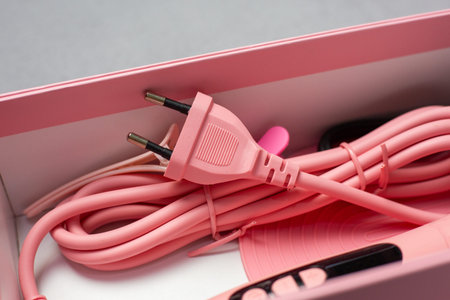 Pink power cord with a two-prong plug and various accessories placed inside a light pink box,...