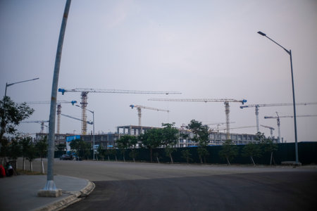 A large construction site featuring multiple tower cranes and unfinished structures, surrounded by greenery and fencing.の写真素材