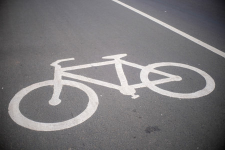 A close-up view of a white bicycle lane symbol painted on an asphalt road. The clean markings emphasize dedicated cycling infrastructure in an urban environment.の写真素材