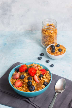 A blue bowl of refreshing and healthy cereal with a mixture of strawberries and blue berries, with a...