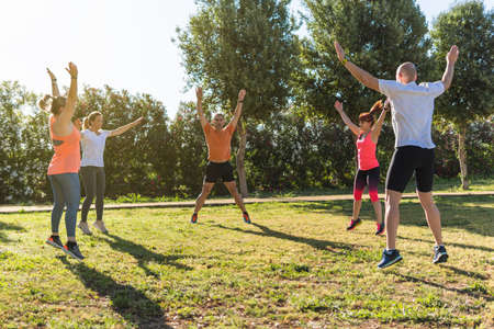Group of people jumping to warm up in a personal training session in the park.