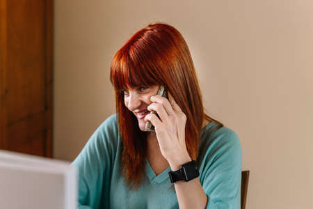 Woman smile while talking with the mobile facing a computer at home