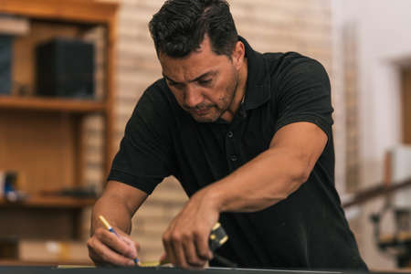 Concentrated man drawing on a surface using a meter in a workshopの写真素材