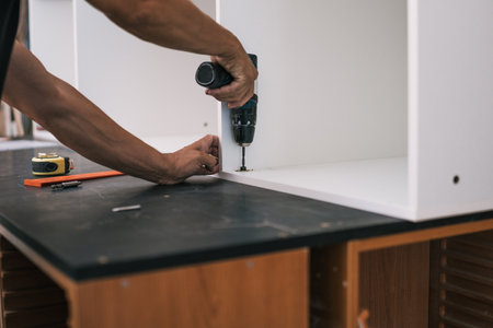 hands nailing a screw with a drill into a white wooden piece of furnitureの写真素材