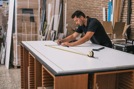 Man marking with pencil the lines to cut on a panel in a workshopの写真素材