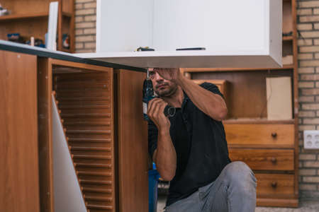 Worker drilling a hole under a board in a workshop.の写真素材