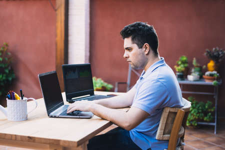 man sitting on a garden terrace using two laptops to trade in cryptocurrenciesの写真素材
