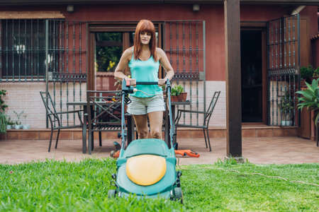 red-hair woman cutting the lawn os his garden with a lawn mower