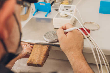 Close-up view of a caucasian adult male using wax to mold a dental mold sitting in a laboratory...