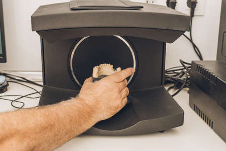 Close-up view of a caucasian adult man's hand introducing a dental mold into a scanner in a...