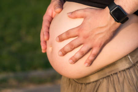 Close-up view of the hands of a man on the abdomen of a pregnant woman outdoorsの写真素材