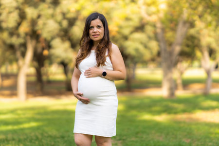 Pregnant woman in a dress standing in a park caressing her bellyの写真素材