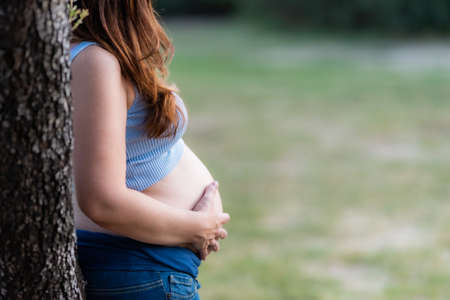 Profile of an unrecognizable pregnant woman leaning on a tree in a parkの写真素材