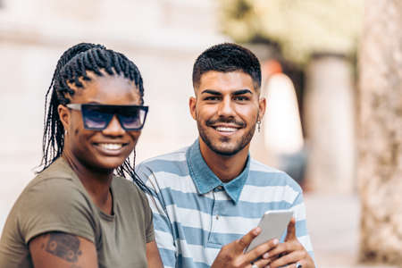 Afro woman and a caucasian man smiling to the camera using a mobile outdoors