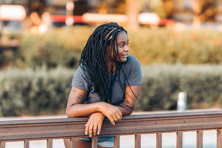 Distracted afro woman with braided hair leaning on a rail in the streetの写真素材