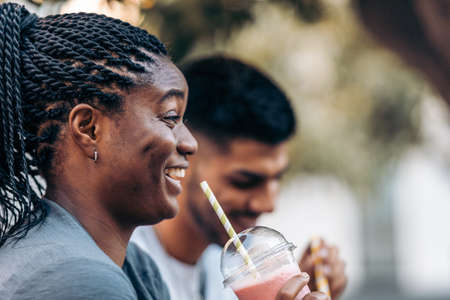 Black young woman smiling while drinking a shake with a caucasian man outdoors