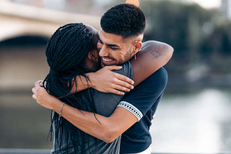 Modern caucasian man hugging an afro woman while smiling outdoorsの写真素材
